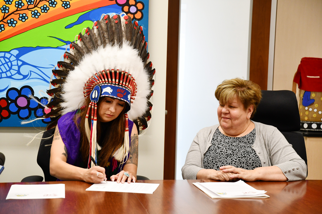 FSIN Third Vice Chief Aly Bear signs an MOU with Pewaseskwan as Alexandra King looks on. The MOU, signed June 24, 2022, will foster stronger research ties between Pewaseskwan and the Saskatchewan First Nations Women’s Commission (SFNWC). (Photo by Sarah MacDonald)
