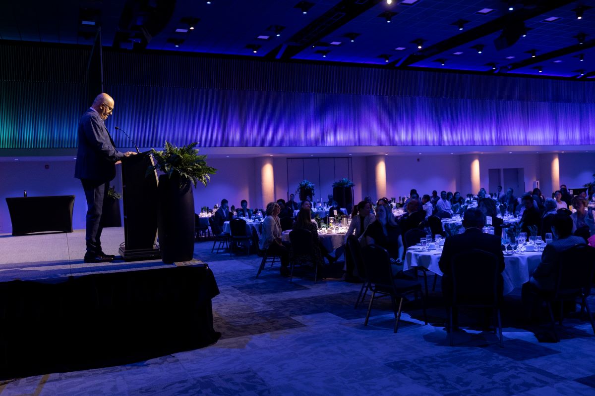 Dr. Haddad stands on stage speaking to a crowd seated at tables.