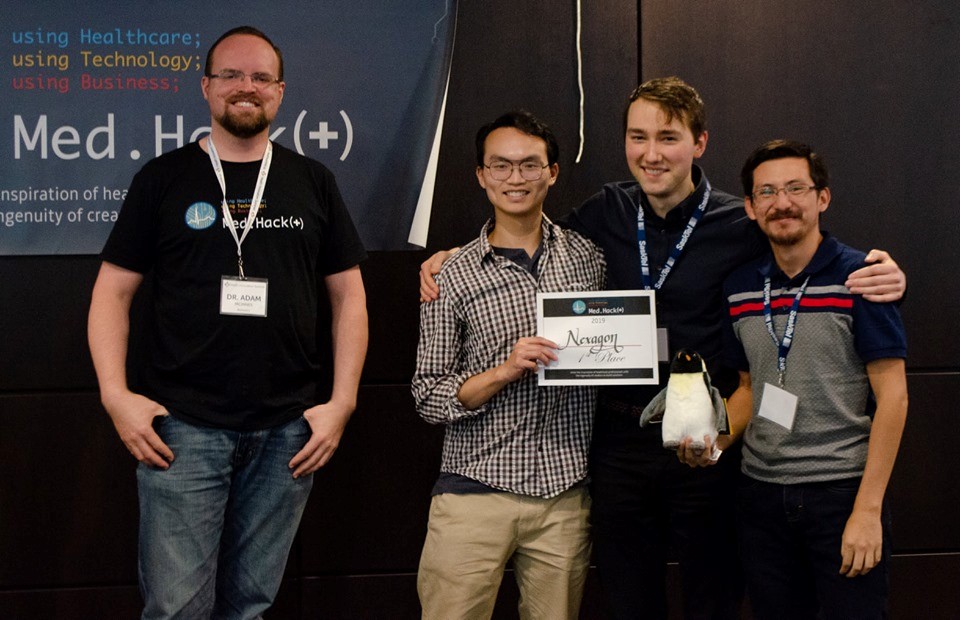 Dr. Adam McInnes (MD) president and co-chair of Med.Hack(+) presents USask medical students Richard Ngo, Brandon Spink and biomedical engineering student Andres S. Erazo with a first place certificate and the First Penguin Award at the 2019 Med.Hack(+) competition. 