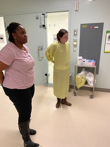 First-year medical student Maa Quartey and third-year student Megan Gallagher receive training on how to coach proper donning and doffing techniques. 