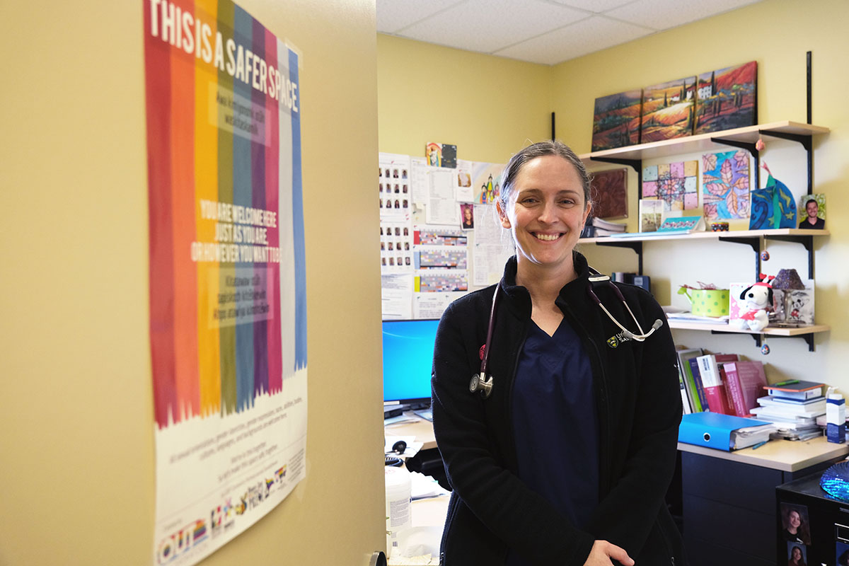Dr. Carla Holinaty (MD), family physician at West Winds Primary Health Centre and assistant professor in the Department of Academic Family Medicine stands next to a poster advocating for safe spaces. (Photo: Jana Al-Sagheer)