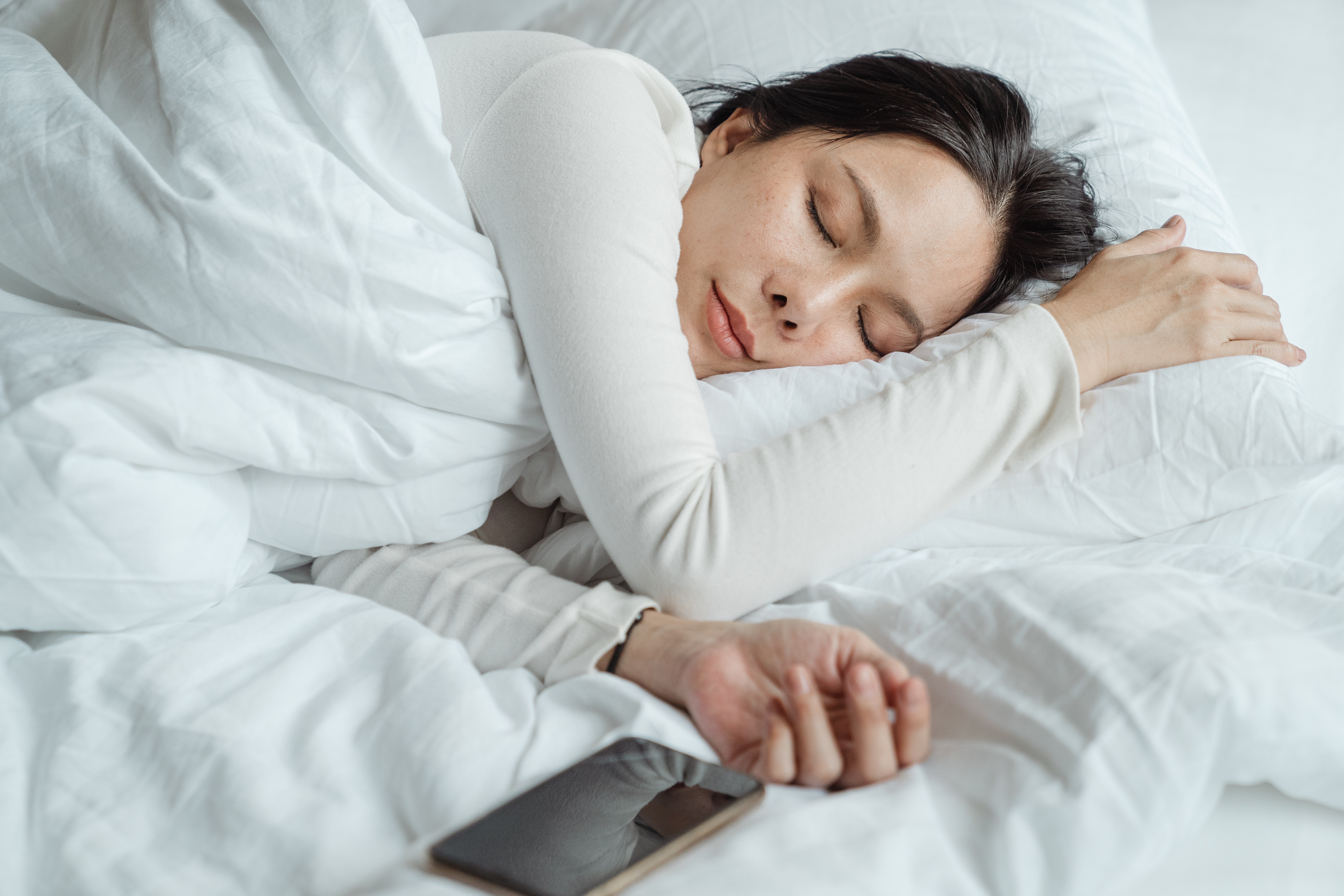 Woman sleeping on bed with phone next to her.